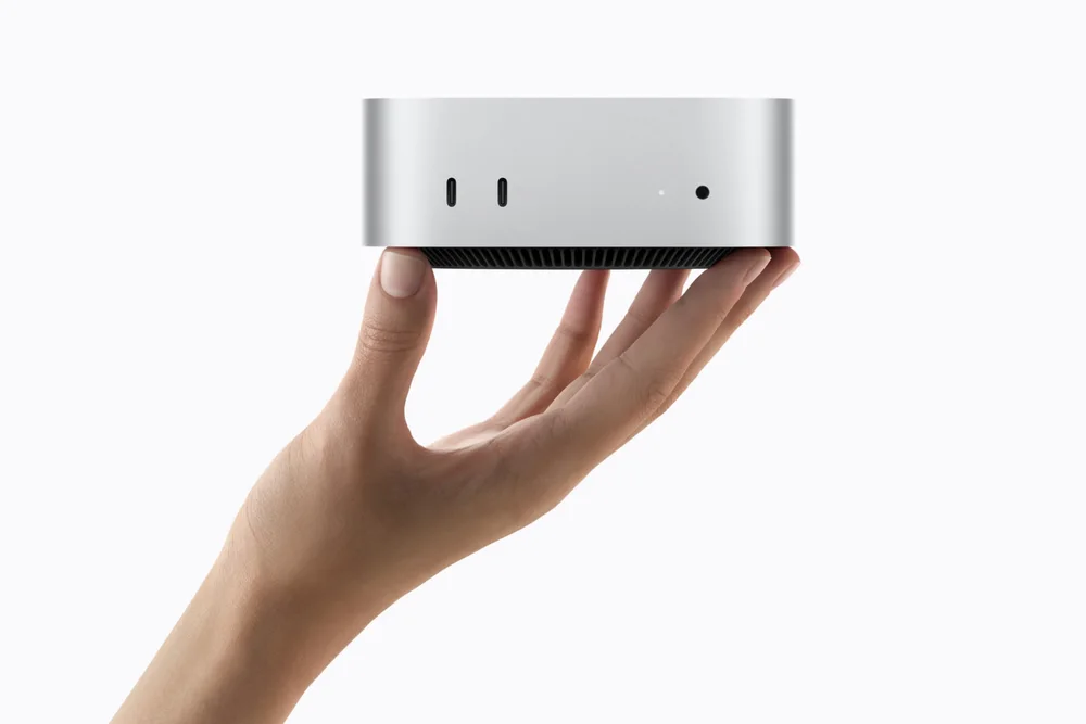 Silver 2026 Mac mini held in one hand, showing its front USB-C ports and headphone jack
